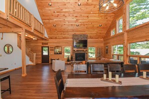 A spacious wooden cabin interior with a fireplace, dining area, and large windows offering views of the outdoors.
