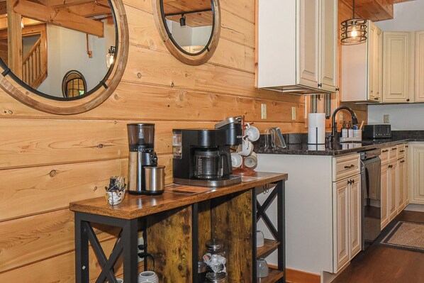 A kitchen with wooden walls, a coffee station, and a view of the living area.