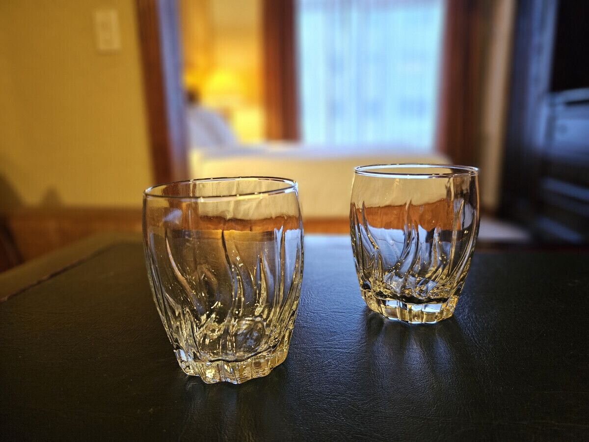 Två klara glas på en mörk yta, med en suddig bakgrund som antyder ett rum med ett fönster och gardiner.