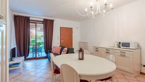 Ein Essbereich mit einem runden Tisch, Stühlen, einer Kandelaber, einem Fernseher und einer Küchenzeile mit einer Mikrowelle.