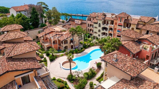 Ein Küstenhotel mit Schwimmbad, umgeben von Gebäuden mit Terrakotta-Dächern, Blick auf das Meer und eine entfernte Insel.