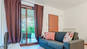 Ein Wohnzimmer mit einer Couch, einem Fernseher auf einem Schrank und einer Schiebetür zu einem Außenbereich.