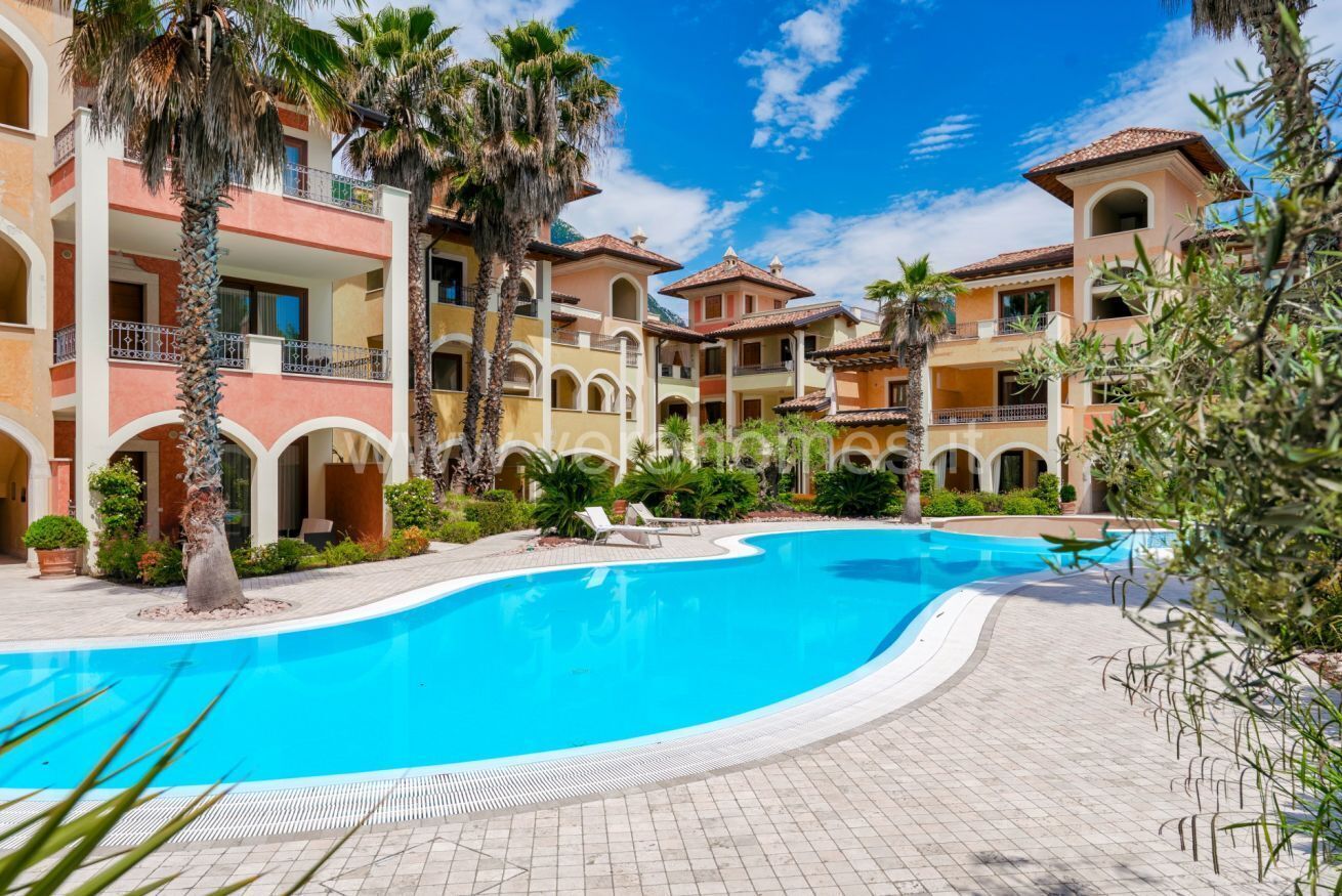 A hotel with a swimming pool, palm trees, and a courtyard with lounge chairs.