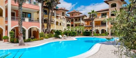 A hotel with a swimming pool, palm trees, and a courtyard with lounge chairs.