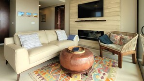 A living room with a beige sofa, a wooden coffee table, a wicker chair, a ceiling fan, and a flat-screen TV mounted on the wall. - Lovely Condo with Stunning Ocean View (Playas de Rosarito)