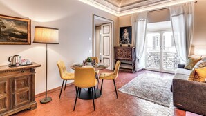 A living room with a dining area, a sofa, a lamp, a painting, and a view through a door. - Corso 142 elegant apartment within walking distance of Piazza Navona (Roma)
