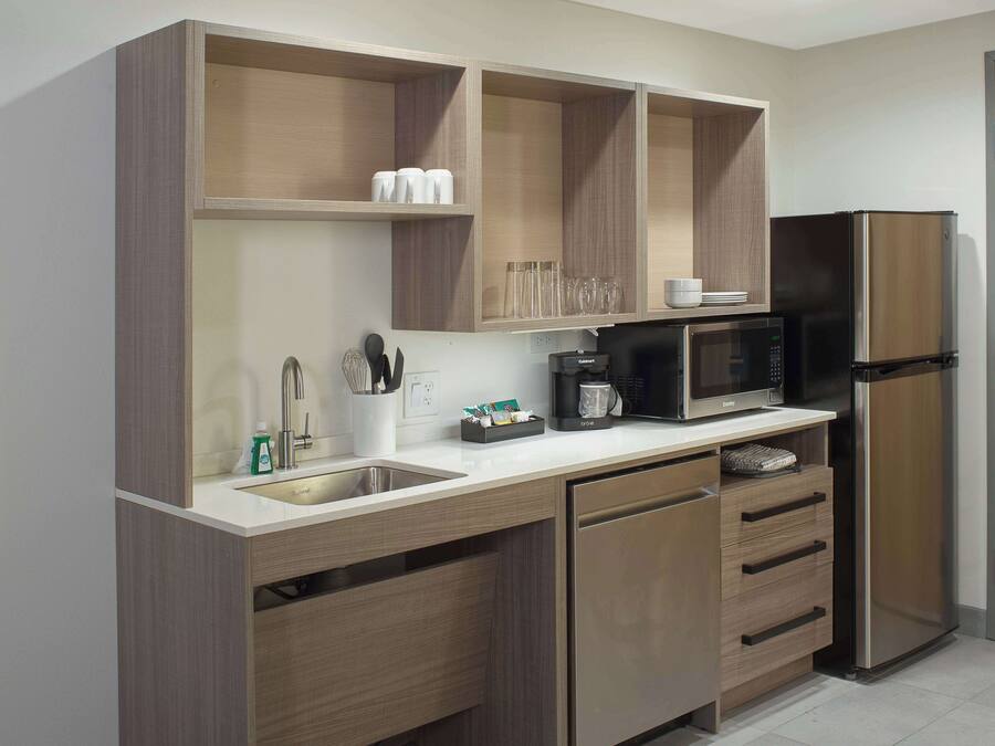 A modern kitchen with wooden cabinets, a stainless steel refrigerator, a microwave, and a sink.