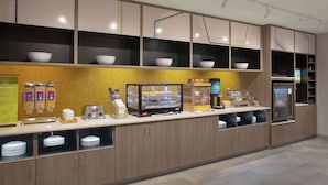 Un área de cocina moderna con zona de autoservicio, que incluye una cafetera, un tostador y tazones sobre estantes.