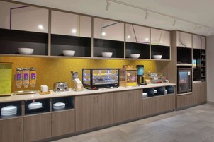 Un área de cocina moderna con zona de autoservicio, que incluye una cafetera, un tostador y tazones sobre estantes.