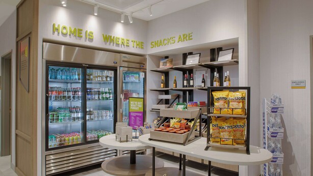 Una presentación de aperitivos con un cartel que dice 'Home is where the snacks are', una zona refrigerada para bebidas y un cartel con la palabra 'hello' sobre una mesa.