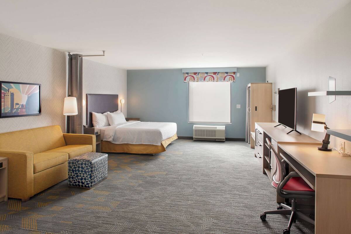 A hotel room with a bed, a sofa, a desk, and a TV.