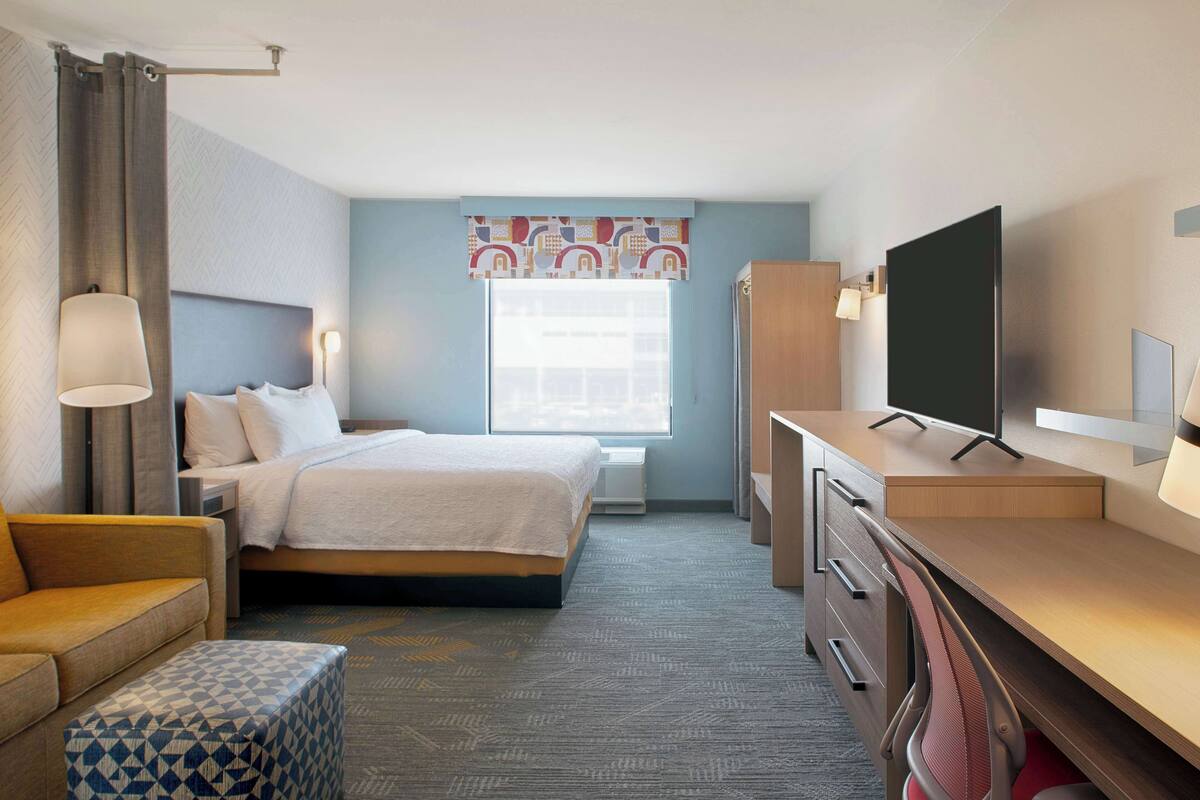 A hotel room with a bed, a desk, a chair, a TV, and a window with curtains.