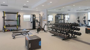 Un gimnasio con equipo de levantamiento de pesas, cintas de correr y un espejo grande.