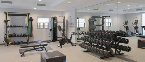 Ein Fitnessstudio mit Gewichte, Laufbändern und einer Spiegelwand.