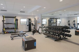 Un gimnasio con equipo de levantamiento de pesas, cintas de correr y un espejo grande.