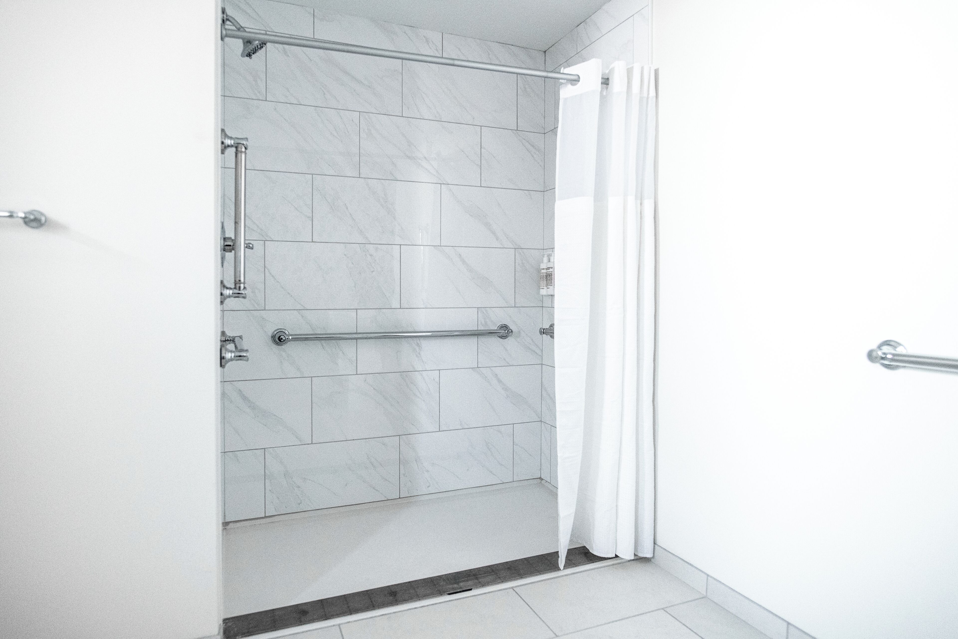 Une salle de bain moderne avec un espace douche, des barres d’appui et un rideau blanc.