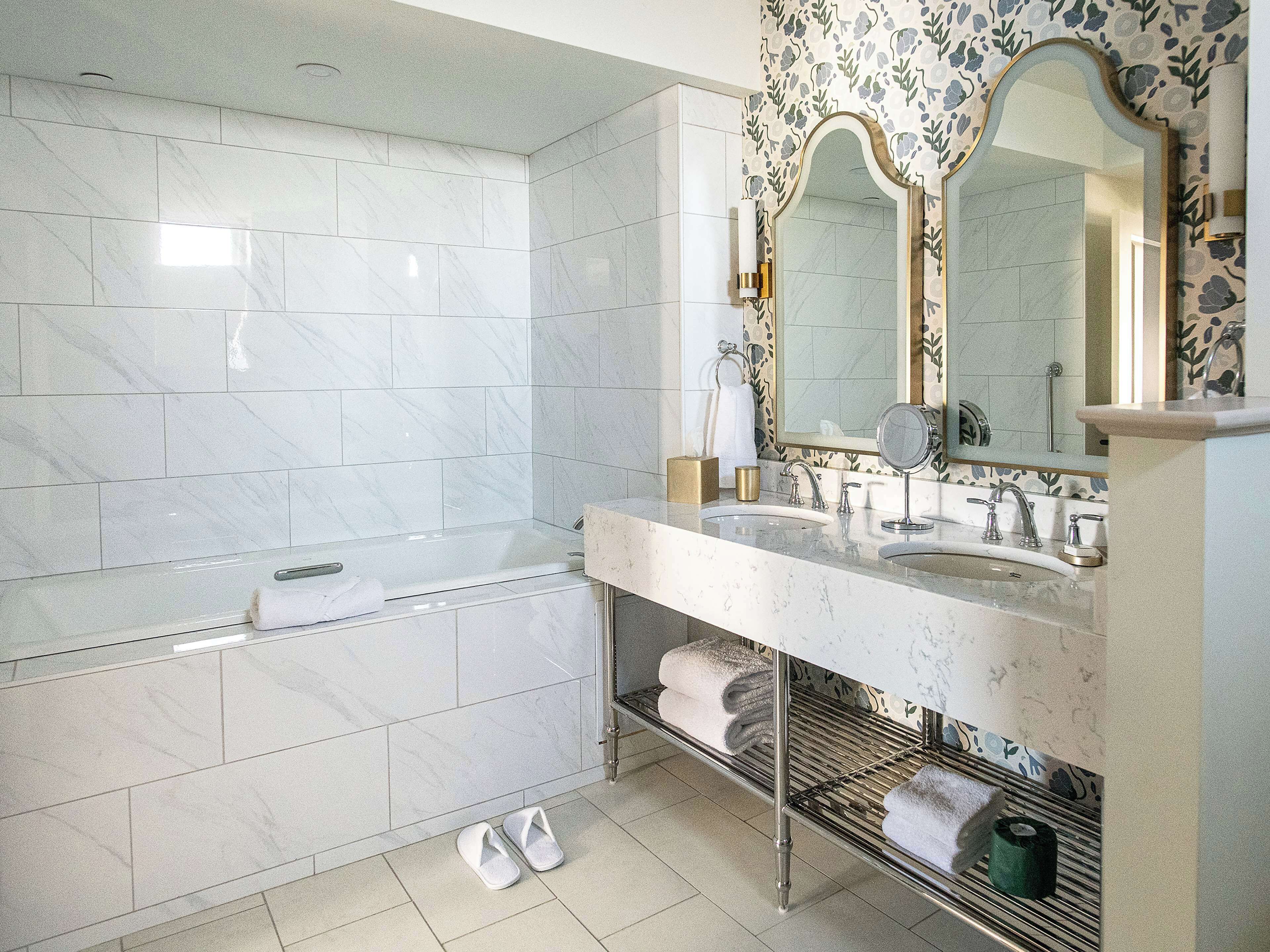 A bathroom with a bathtub, two sinks, a vanity with a mirror, and a towel rack.
