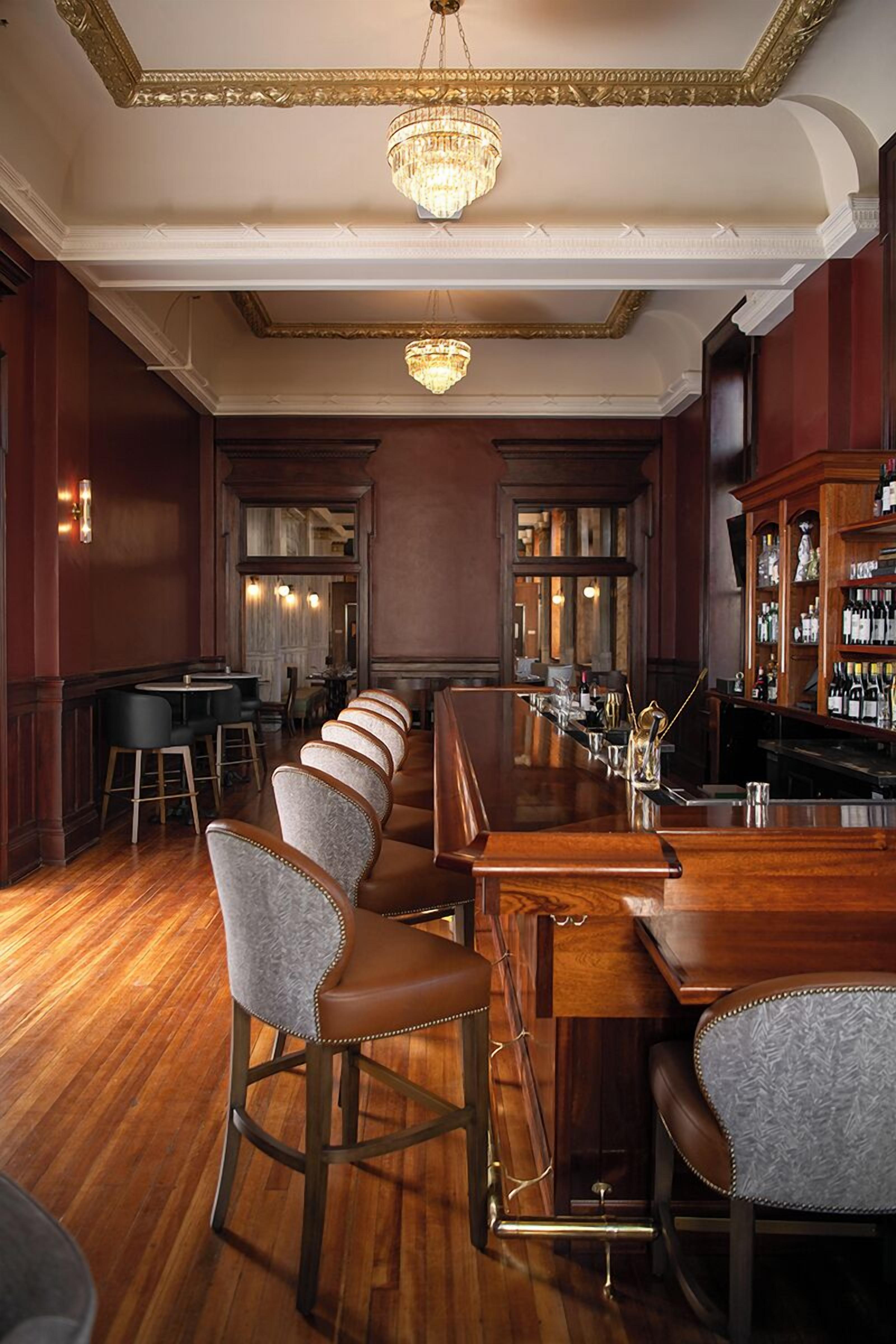 Un espace bar doté d’un long comptoir, de tabourets de bar et d’un lustre.