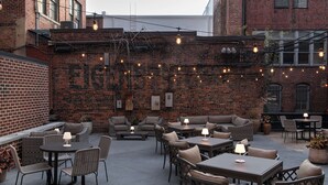 Un patio exterior con paredes de ladrillo, muebles de mimbre e iluminación con guirnaldas.