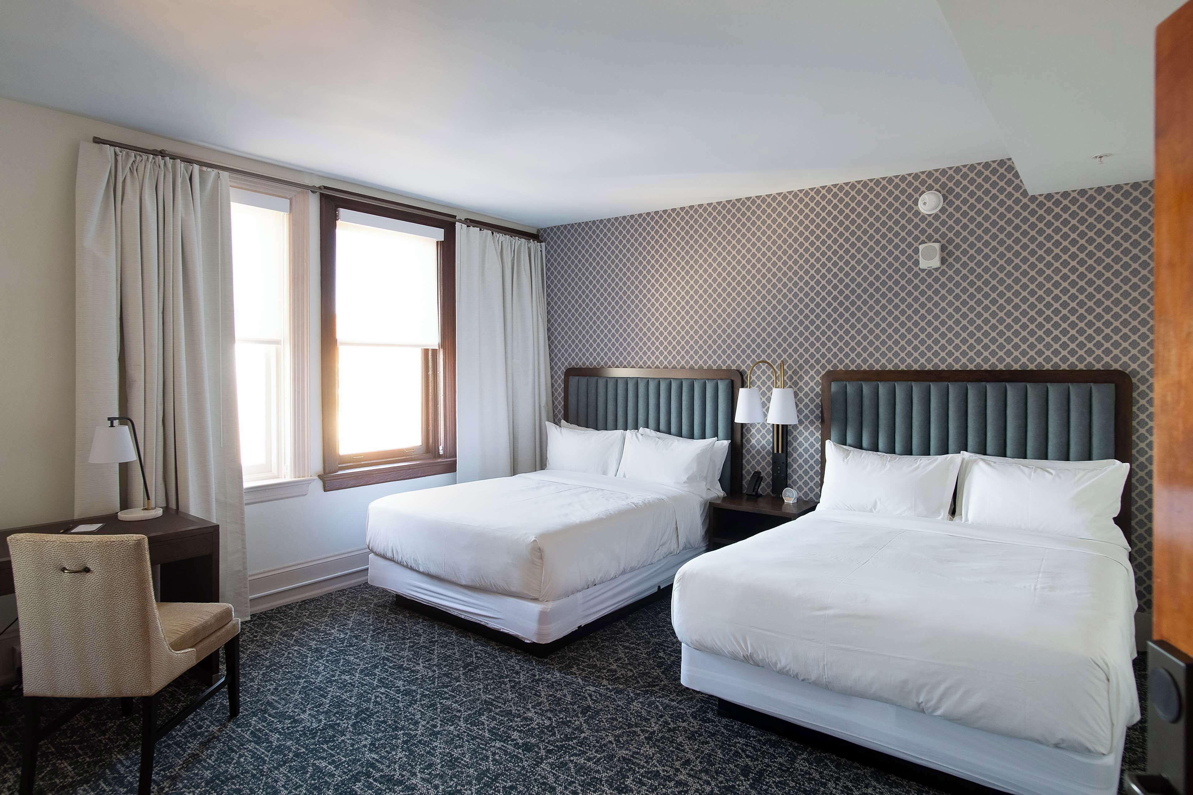 A hotel room with two beds, a desk, a chair, and a window with curtains.