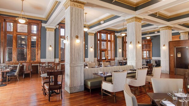 Un restaurante espacioso con techos altos, columnas de mármol y suelo de madera.