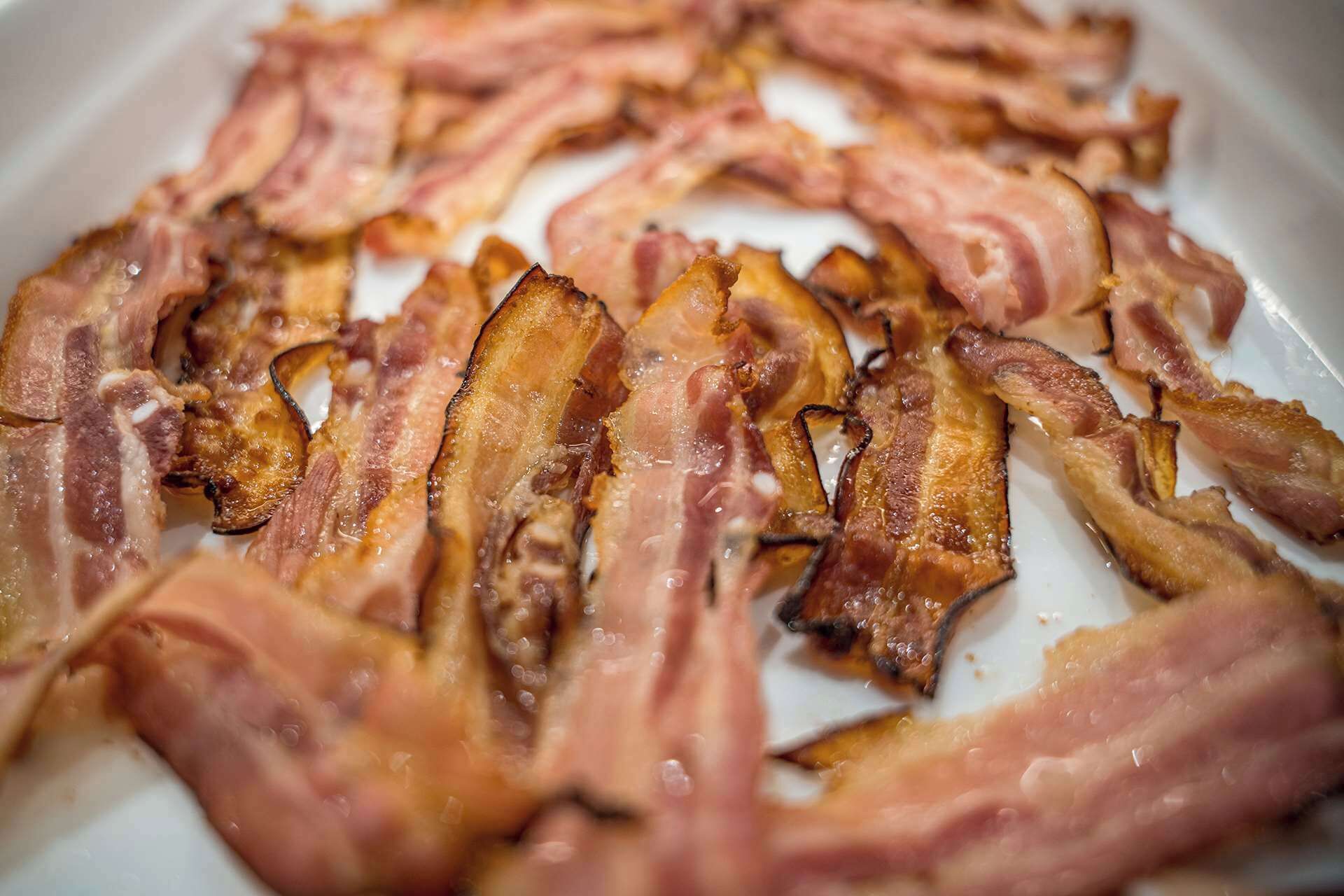 A close-up of cooked bacon strips on a white plate.