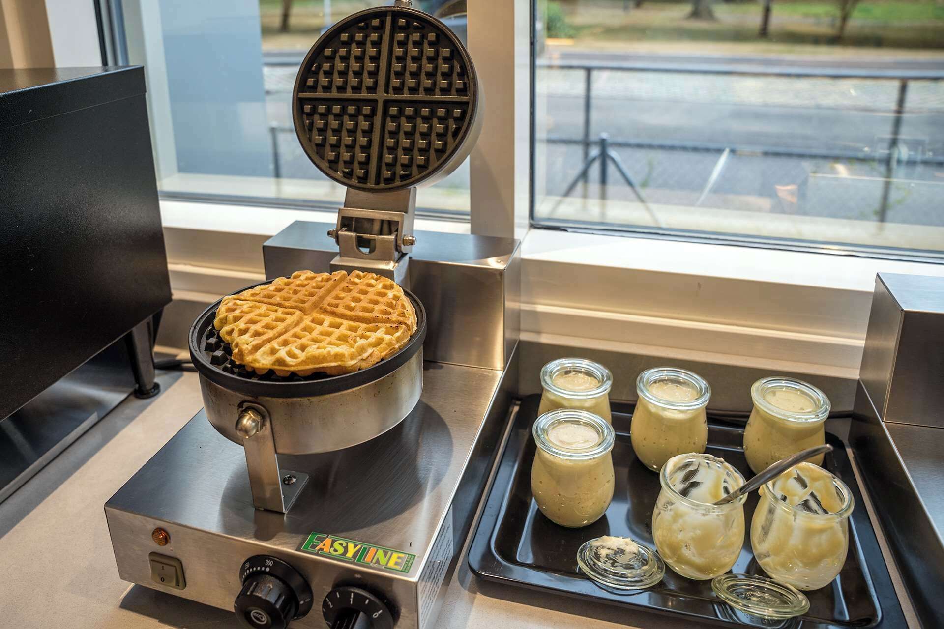 Vohvelirauta, jonka sisällä on vohveli, sekä useita siirappipurkkeja tarjottimella.