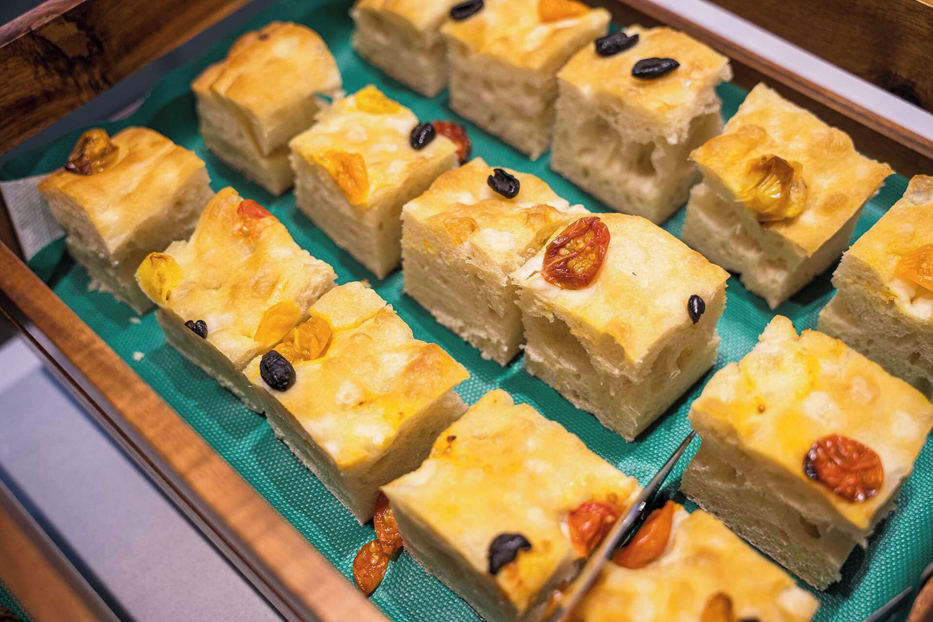 Een schaal met vierkante gebakjes, met een goudbruine korst, waarvan sommige belegd zijn met gedroogd fruit en noten.