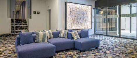 A modern lobby with a blue sectional sofa, patterned carpet, and a large abstract artwork.