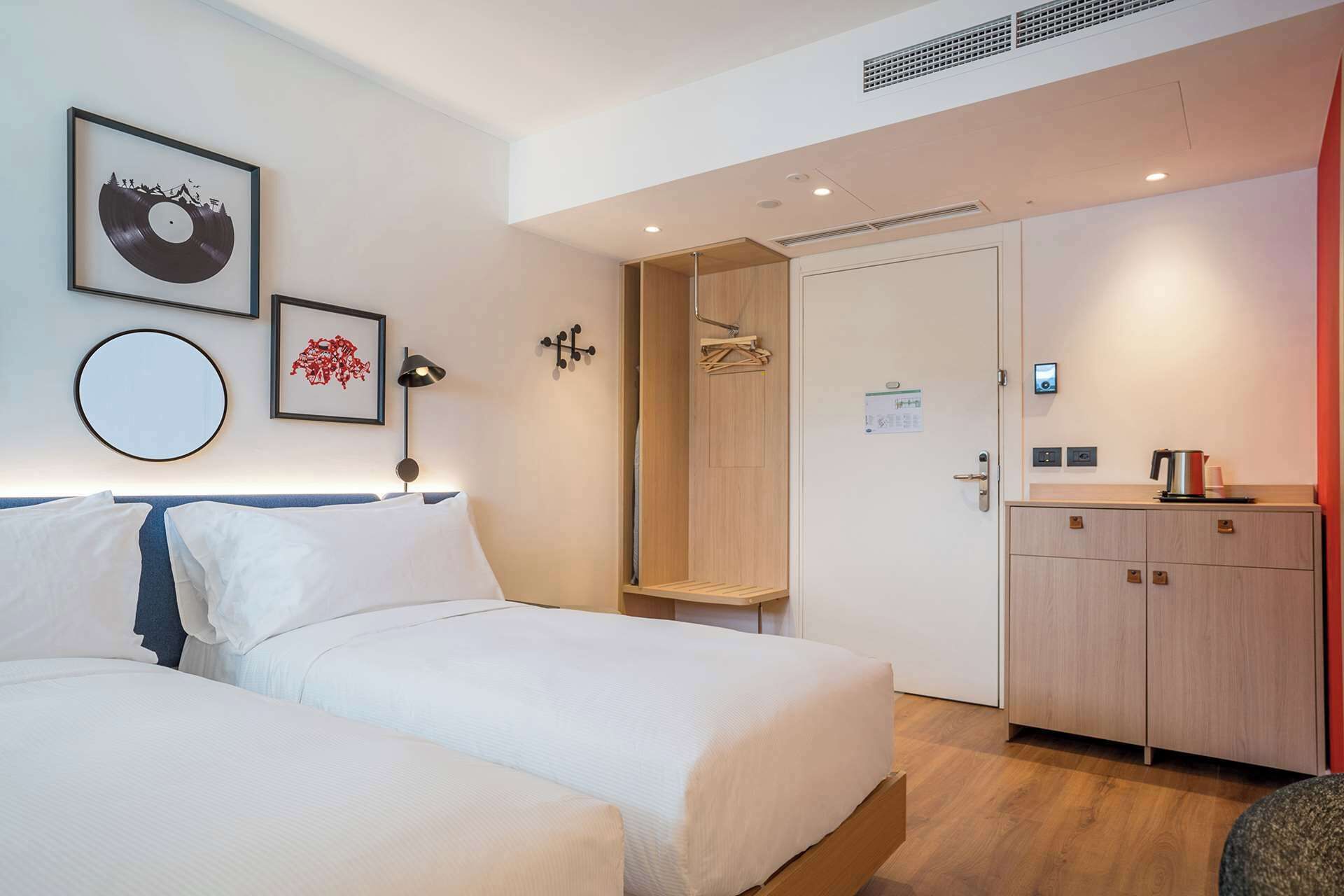 A hotel room with two beds, a wooden wardrobe, a shower area, and a small kitchenette.