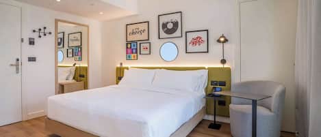 A modern hotel room with a large bed, bedside tables, a chair, and wall art.
