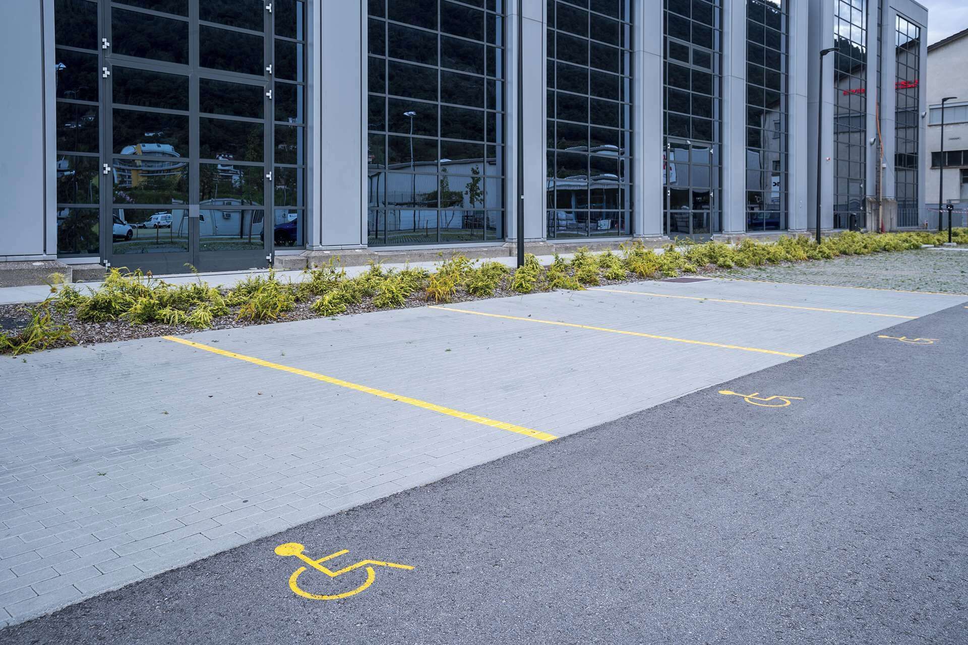 Un espace de stationnement avec des places délimitées, dont une place réservée aux personnes handicapées, situé devant un bâtiment moderne doté de grandes fenêtres.