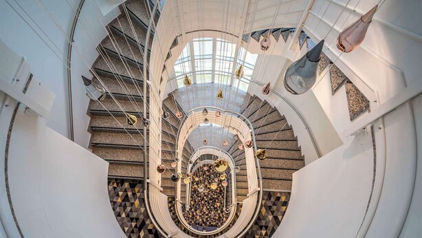 A spiral staircase with a geometric patterned floor, metal railings, and pendant lighting. - Hampton By Hilton Locarno (Losone)