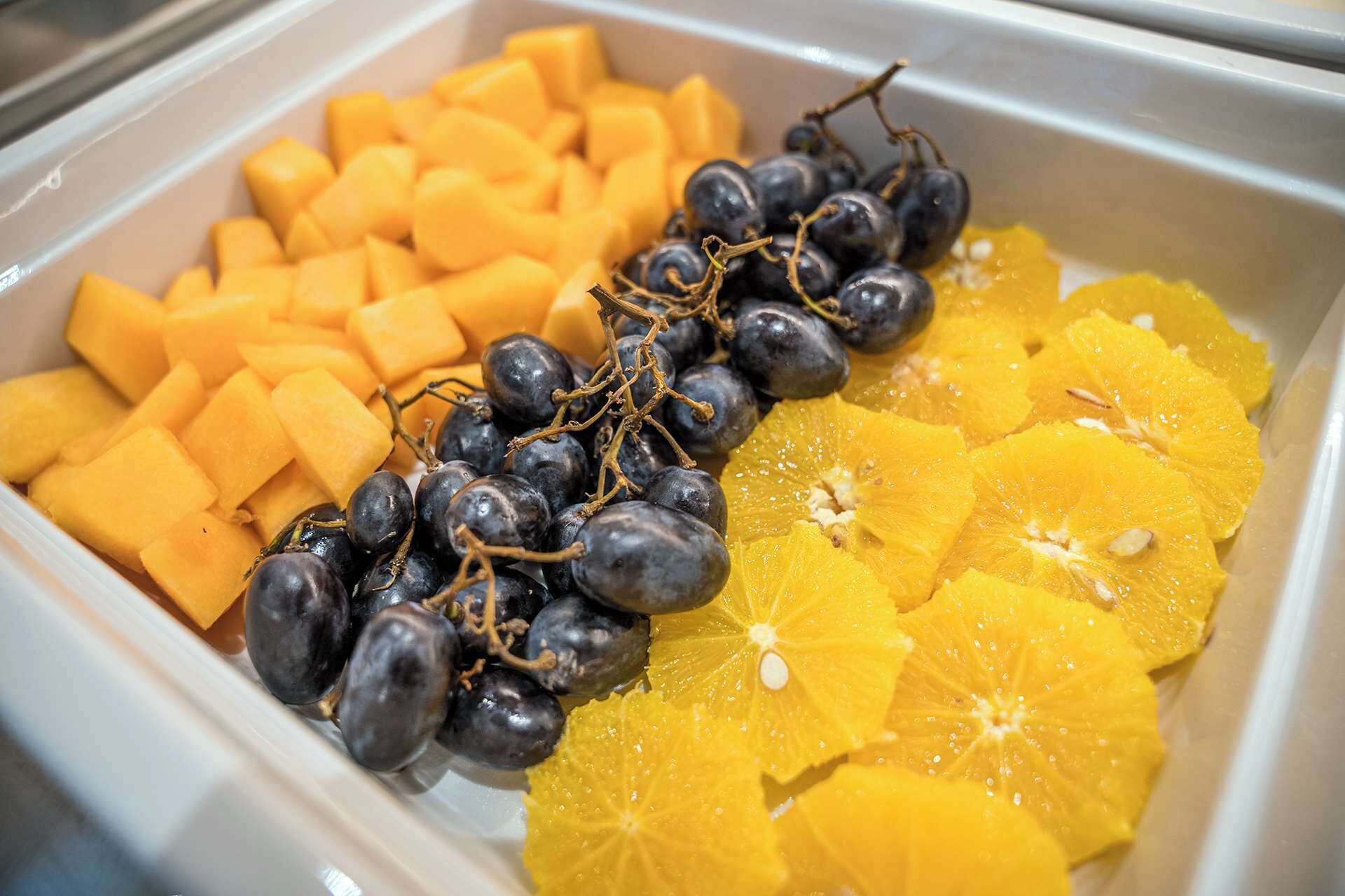Un bufé con cubos de mango, uvas enteras y rodajas de naranja.