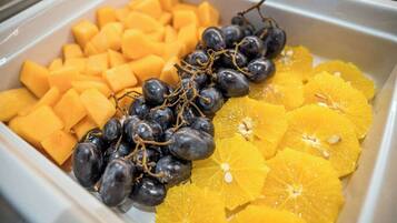 Un bufé con cubos de mango, uvas enteras y rodajas de naranja.
