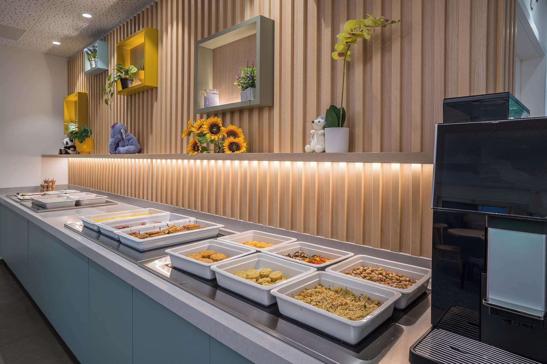 Un'area buffet con diverse opzioni gastronomiche, un televisore e piante ornamentali.
