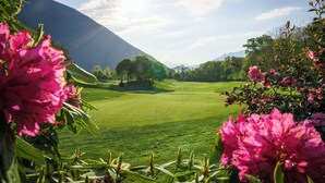 A golf course with a clear view of the green, trees, and a distant mountain. - Hampton By Hilton Locarno (Losone)
