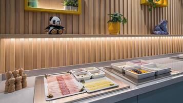 A buffet with various food items, including meats and fruits, and decorative elements like a panda plush toy and potted plants.