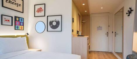 A hotel room with a bed, a small kitchenette, a door with a sign, and a wall with framed pictures.