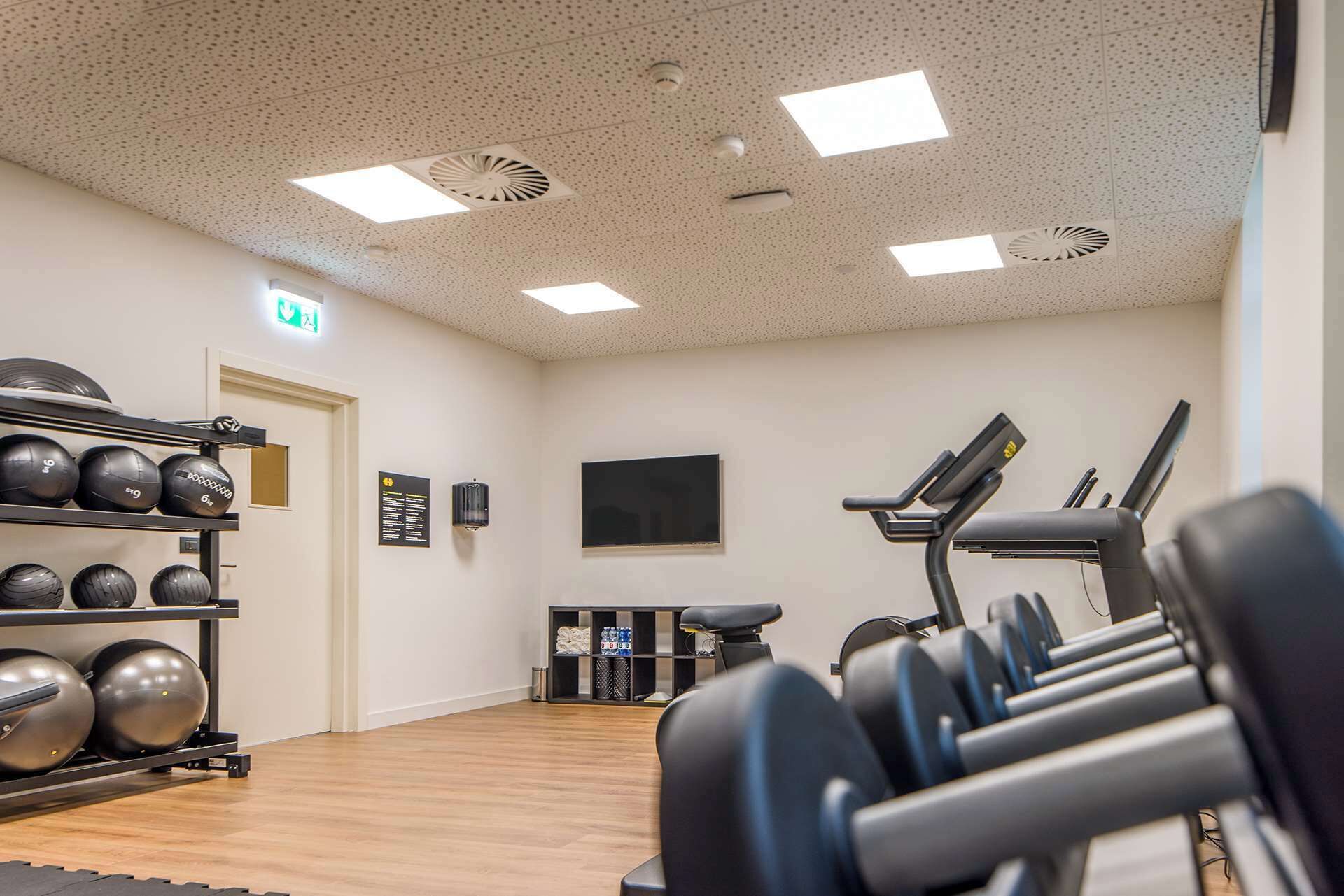 A gym with exercise equipment, a treadmill, and a wall-mounted TV.