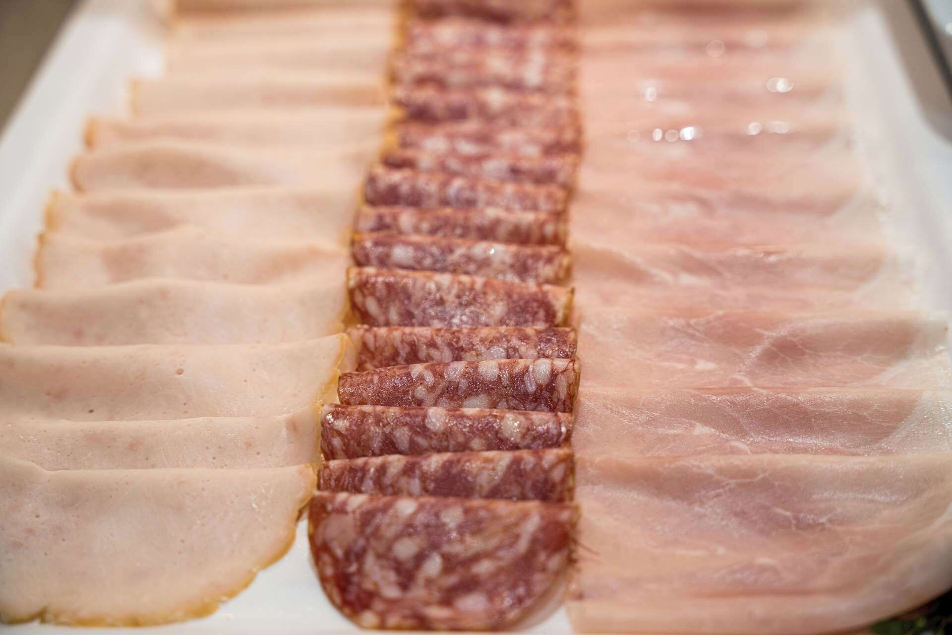 Una exhibición de embutidos en rodajas, que parece incluir jamón y quizás salami, dispuestos en fila sobre una superficie blanca.