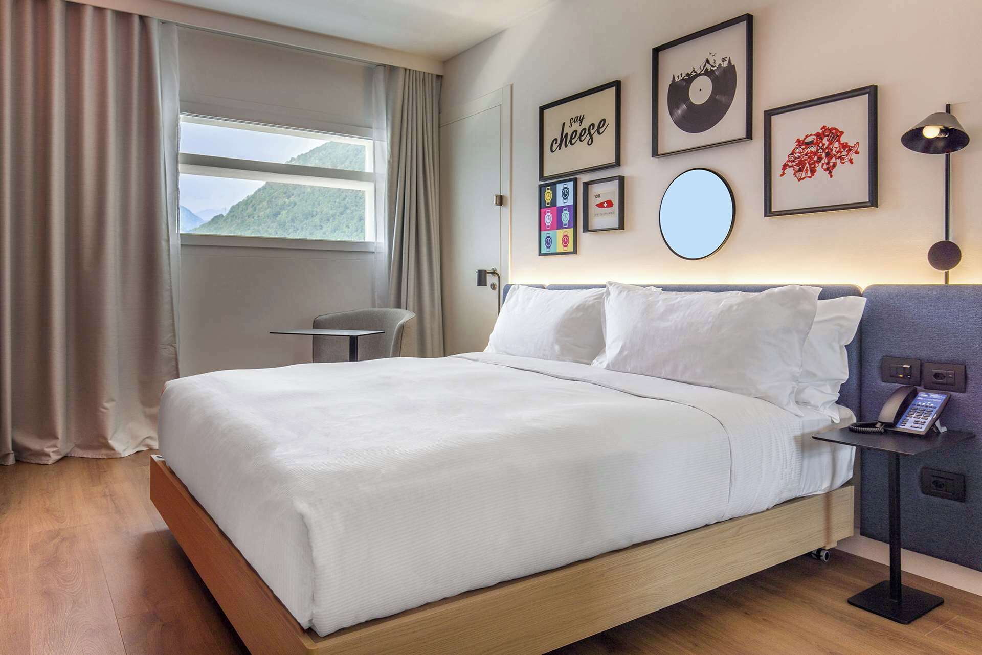 A hotel room with a bed, a desk, a chair, and a view of the outdoors.