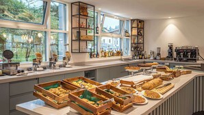 A breakfast buffet with various pastries and bread, a coffee machine, and shelves with bottles and glasses. - Hampton By Hilton Locarno (Losone)