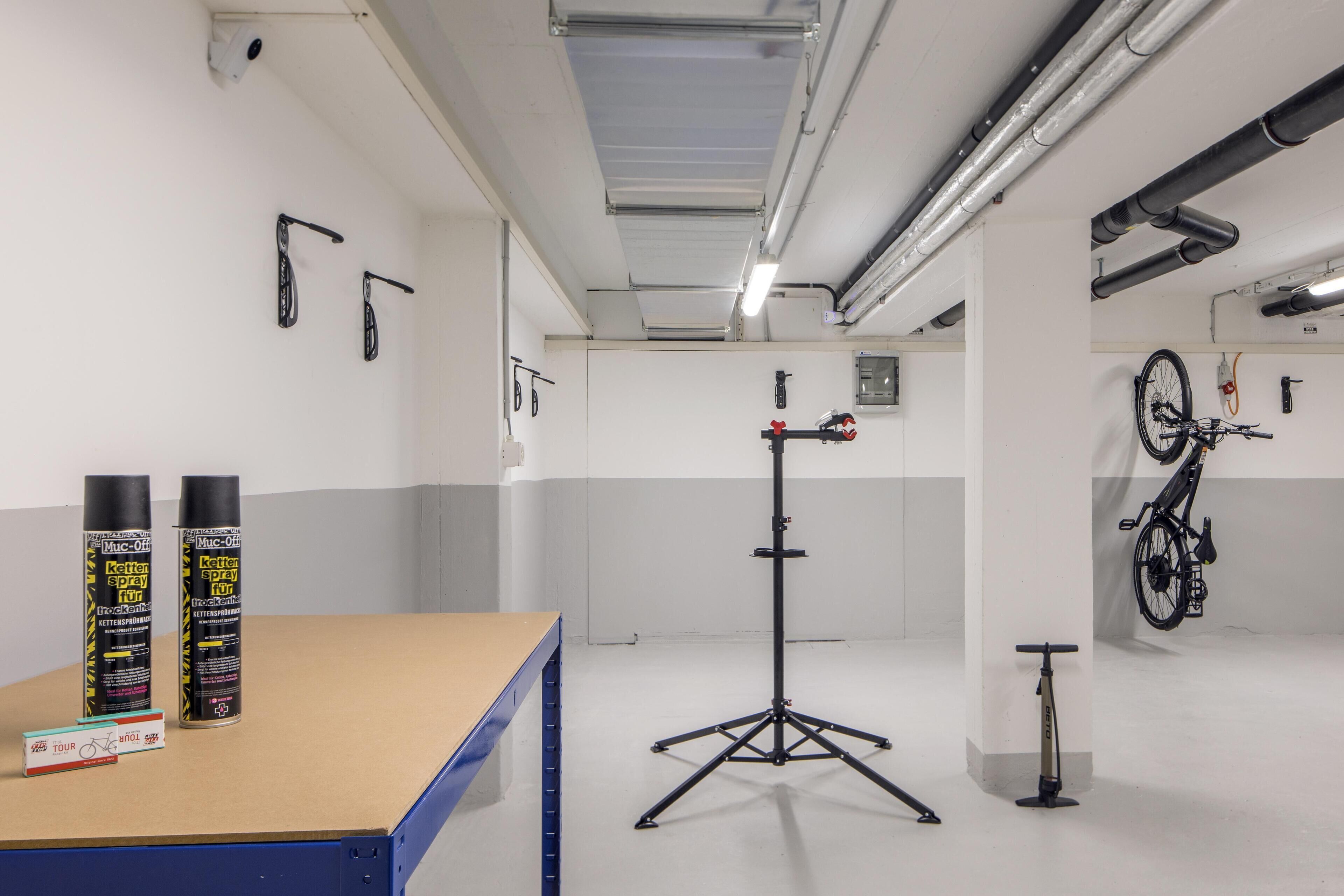A clean, well-lit indoor space with a table holding items, a tripod stand, and a bicycle mounted on the wall.