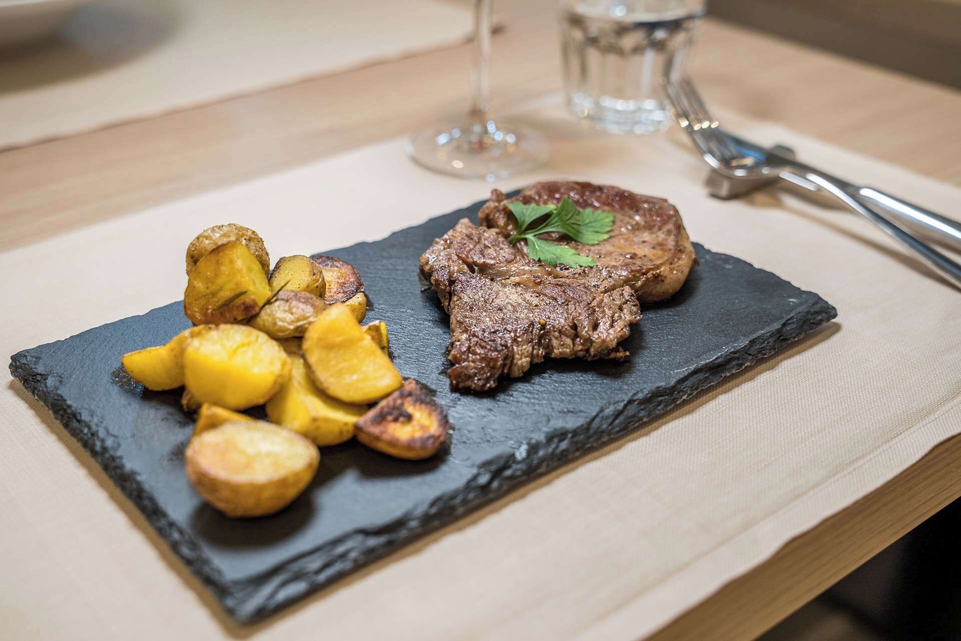 Un plato de carne a la parrilla y patatas asadas sobre una tabla de pizarra.