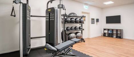 A gym with a weight machine, a bench, and a rack of medicine balls.
