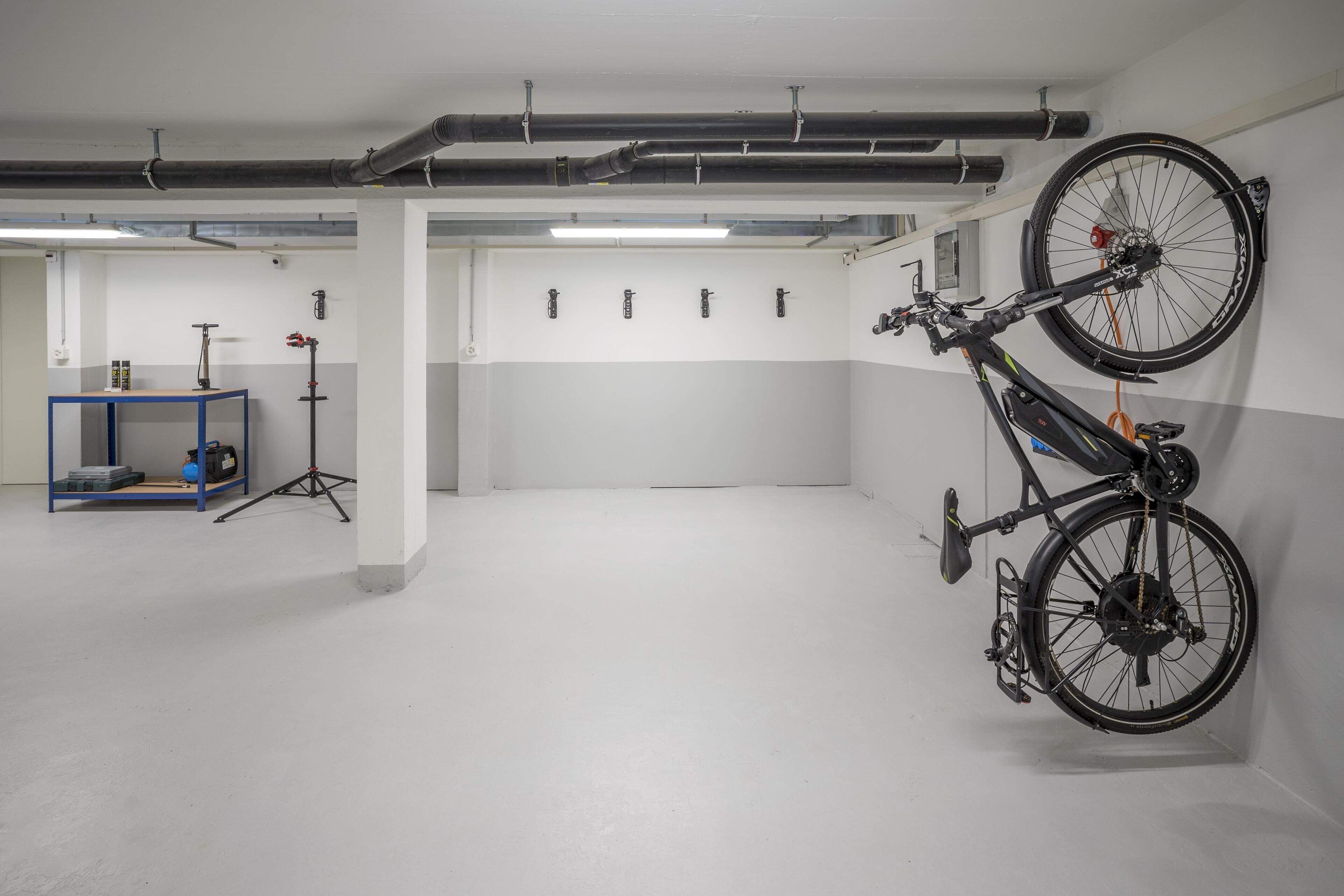 Ein großzügiger Innenbereich mit einem an der Wand befestigten Fahrrad, einem blauen Tisch mit Geräten und einem weißen Boden.