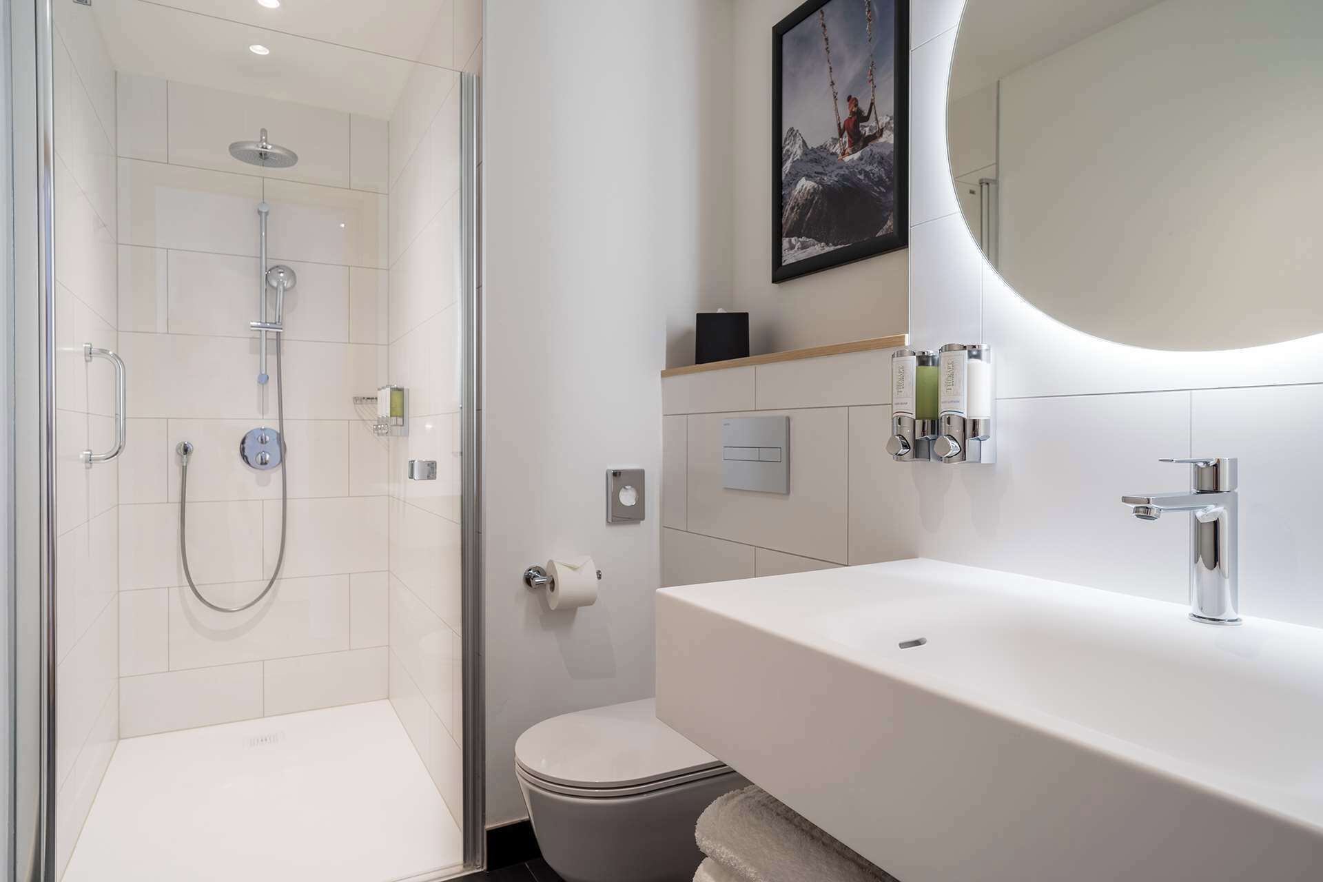 Un baño moderno con ducha envuelta en vidrio, un lavabo blanco y un espejo grande.