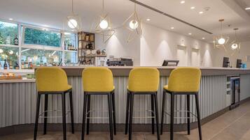 A modern bar area with four yellow barstools, a bar counter, and pendant lighting.