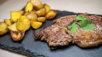 Ein Steak mit Garnitur auf einer Schieferplatte, dazu Bratkartoffeln.